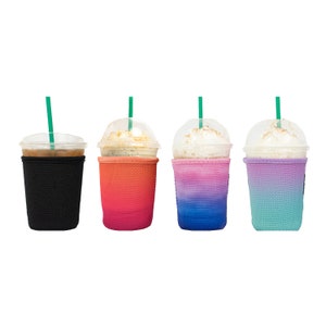 May include: Four iced coffee drinks in clear plastic cups with green straws. Each cup is in a different colored sleeve: black, orange to red gradient, pink to blue gradient, and purple to teal gradient. The drinks have whipped cream.