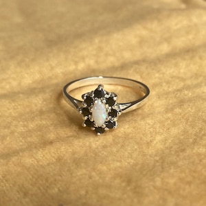 May include: A silver ring featuring a white opal gemstone set in a halo of black stones.