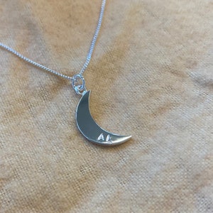 May include: A silver necklace with a crescent moon pendant. The pendant has the initials "AL" engraved on it.