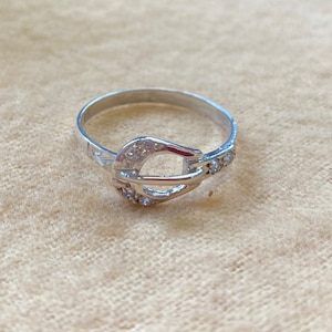 Op de afbeelding: Een zilveren ring met een helder kristal gesp ontwerp. De ring is eenvoudig en elegant.