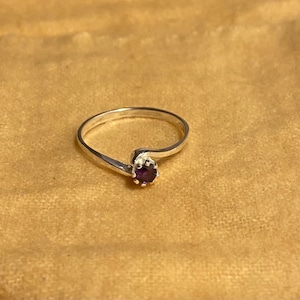 May include: A silver ring with a small, round, purple gemstone set in a prong setting.