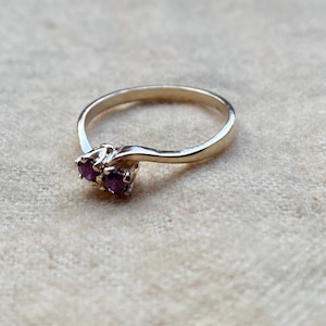 May include: A gold ring with two small purple gemstones set in a twisted band.
