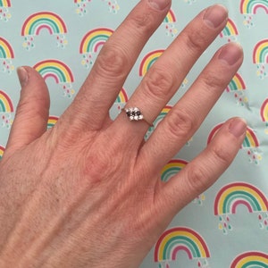 Könnte beinhalten: Ein silberner Ring mit einem Cluster aus kleinen schwarzen und weißen Steinen. Der Ring befindet sich an einem Finger.