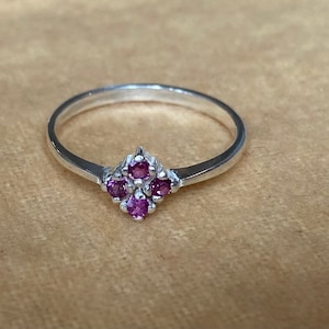 May include: A silver ring with a cluster of five small pink gemstones set in a diamond shape.