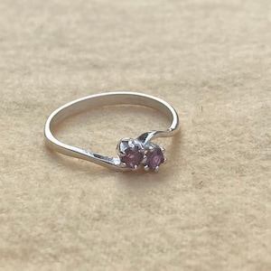 May include: A silver ring with two small purple gemstones set in a twisted band.