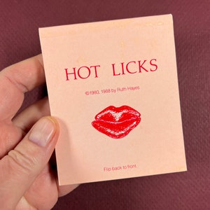 May include: A pink card with the text "HOT LICKS" in red letters. The card also includes the text "©1980, 1988 by Ruth Hayes" and a red drawing of a pair of lips. The bottom of the card reads "Flip back to front."