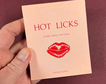May include: A pink card with the text "HOT LICKS" in red letters. The card also includes the text "©1980, 1988 by Ruth Hayes" and a red drawing of a pair of lips. The bottom of the card reads "Flip back to front."