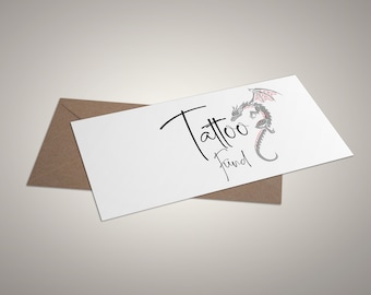 May include: A white card with the words "Tattoo Fund" in black script, accompanied by a gray and red dragon illustration. The card rests on a brown envelope, set against a neutral background.