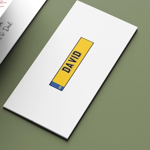May include: A white card with a yellow rectangle displaying the name "DAVID" in black. The rectangle includes a blue section with "GB". The card is on a green surface.