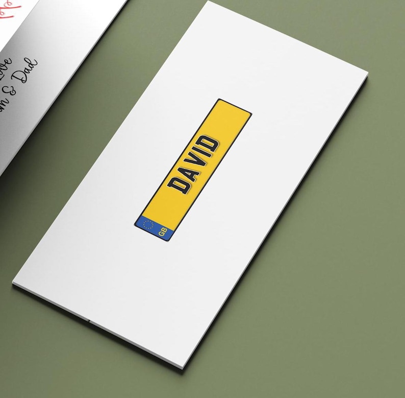 May include: A white card with a yellow rectangle displaying the name "DAVID" in black. The rectangle includes a blue section with "GB". The card is on a green surface.