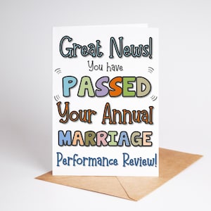 Puede incluir: Tarjeta de felicitaci&oacute;n con el texto "Great News! You have PASSED Your Annual MARRIAGE Performance Review!" en letras coloridas. La tarjeta est&aacute; sobre un sobre marr&oacute;n sobre un fondo blanco.