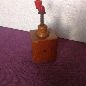 May include: A wooden nutcracker with a red and orange plastic handle and a spring mechanism. The nutcracker is sitting on a purple surface.