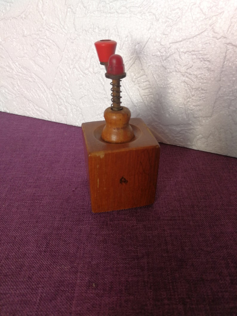 May include: A wooden nutcracker with a red and orange plastic handle and a spring mechanism. The nutcracker is sitting on a purple surface.