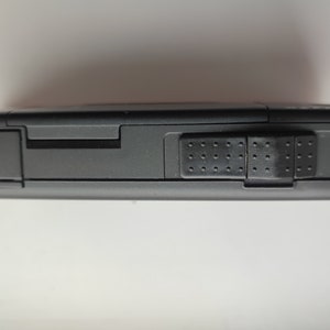 May include: A black, rectangular, electronic device with a textured button on the side.