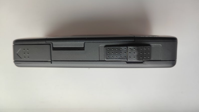 May include: A black, rectangular, electronic device with a textured button on the side.