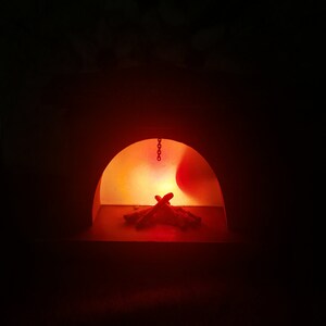 May include: A dimly lit, arched structure with a fiery interior. A small pile of wooden logs is illuminated by a bright orange glow, suggesting a fireplace or oven. A chain hangs from the top of the arch.