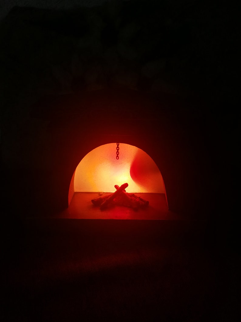 May include: A dimly lit, arched structure with a fiery interior. A small pile of wooden logs is illuminated by a bright orange glow, suggesting a fireplace or oven. A chain hangs from the top of the arch.