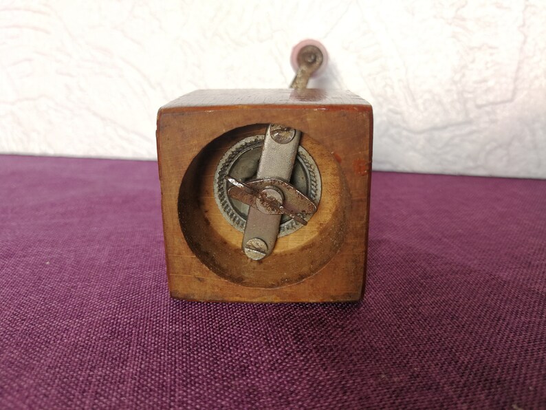 May include: A wooden pepper grinder with a metal grinding mechanism. The grinder has a crank handle and a square base.