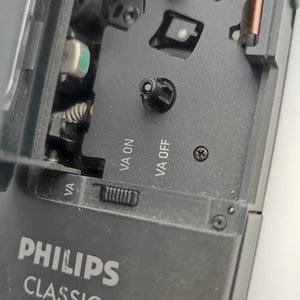 May include: Close-up of a black cassette player with the text "PHILIPS CLASSIC 388" on the front. The player has a cassette tape slot and a volume knob. The text "VA ON" and "VA OFF" are visible on the side of the player.