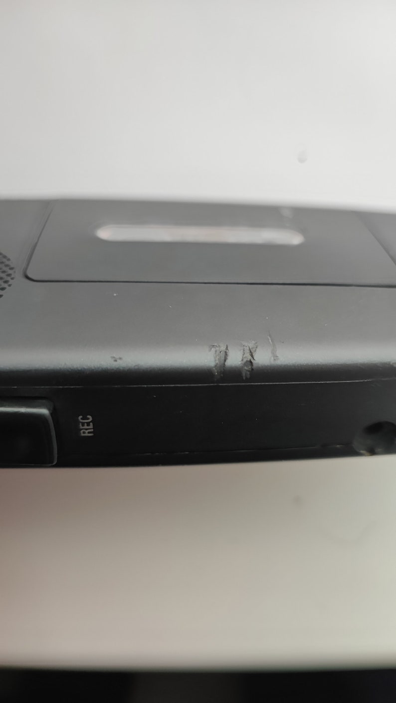 May include: Black cassette player with a silver button labelled "REC" on the side. The player has some scratches on the side.