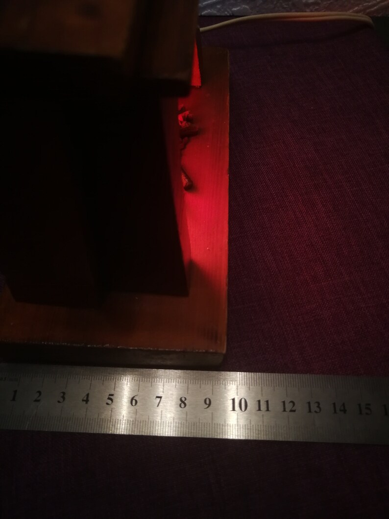 May include: A wooden object with a red glow, possibly a lamp or decorative piece. A metal ruler with inch markings is placed near the object, showing measurements up to 6 inches. The object is on a dark purple surface.