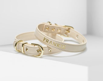 May include: Two beige leather dog collars with gold hardware. The larger collar has the name "FRANKIE" embossed in gold lettering.