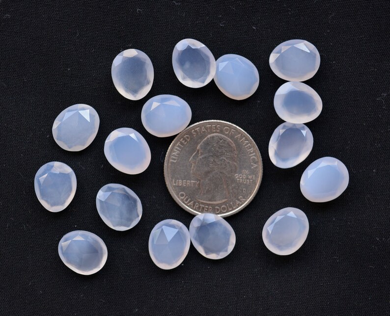 Puede incluir: Un conjunto de gemas ovaladas de color azul p&aacute;lido con superficies facetadas, dispuestas sobre un fondo negro. Se incluye una moneda para comparar el tama&ntilde;o. Las gemas tienen una cualidad transl&uacute;cida.