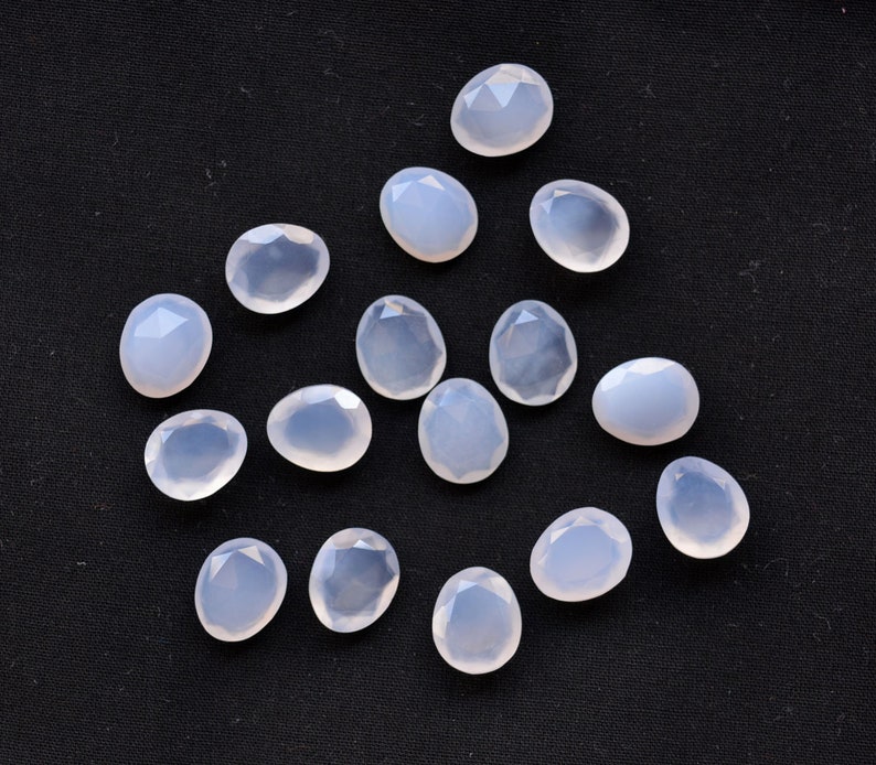 Puede incluir: Una colecci&oacute;n de gemas facetadas de color azul p&aacute;lido, de forma ovalada o de l&aacute;grima. Las gemas est&aacute;n dispersas sobre un fondo negro, mostrando cada piedra un corte &uacute;nico y sutiles variaciones de color y claridad. Ideales para la creaci&oacute;n de joyas.