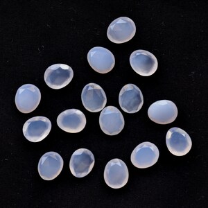 Puede incluir: Un conjunto de gemas facetadas de color azul p&aacute;lido sobre una superficie negra. Las gemas tienen formas variadas, incluyendo &oacute;valos y l&aacute;grimas, y son transl&uacute;cidas. Las facetas capturan la luz, creando un brillo sutil.