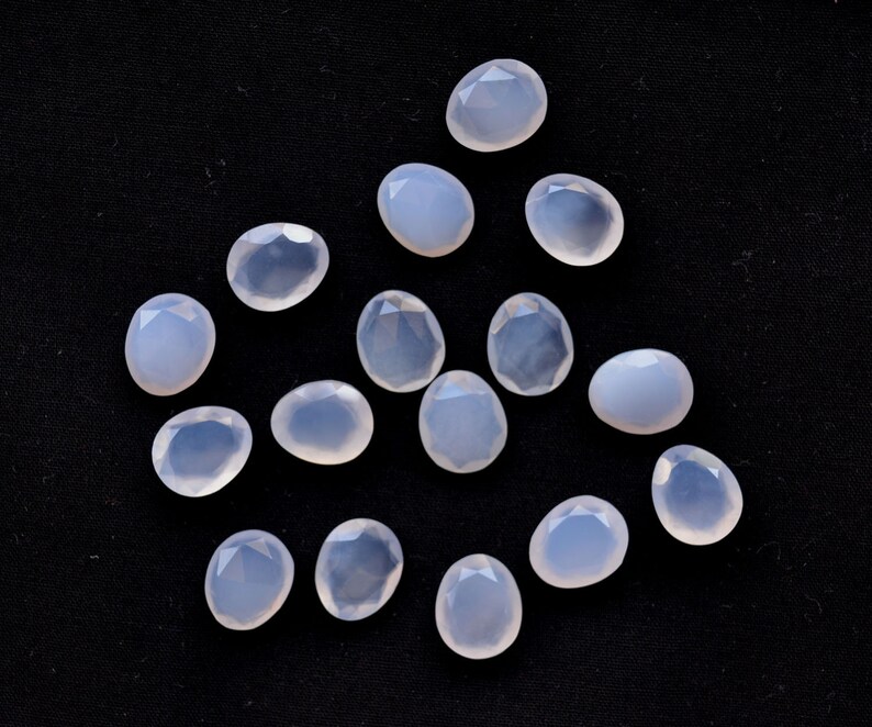 Puede incluir: Un conjunto de gemas facetadas de color azul p&aacute;lido sobre una superficie negra. Las gemas tienen formas variadas, incluyendo &oacute;valos y l&aacute;grimas, y son transl&uacute;cidas. Las facetas capturan la luz, creando un brillo sutil.