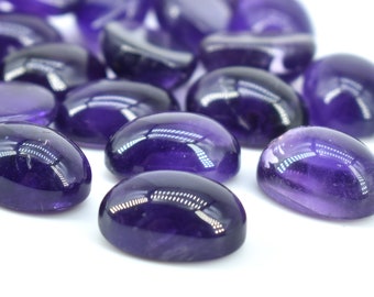May include: A selection of polished, oval amethyst gemstones. The stones are a deep purple colour with a smooth, reflective surface. The gemstones are scattered on a white background, with some in focus and others blurred.