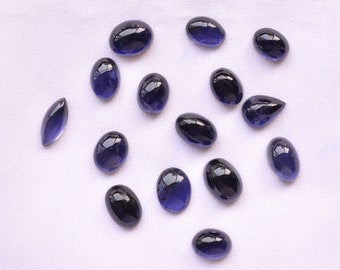 May include: A collection of 15 oval-shaped, dark blue gemstones. The gemstones are arranged in a loose circle on a white fabric background.