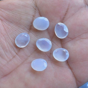 Puede incluir: Seis gemas ovaladas de color azul p&aacute;lido con superficies facetadas se muestran en una mano. Las gemas tienen una calidad transl&uacute;cida, reflejando un tono suave y fresco. Ideal para la creaci&oacute;n de joyas.