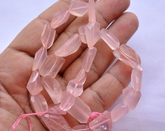 May include: A strand of faceted, light pink rose quartz beads. The beads are irregular in shape, with a polished, translucent appearance. The beads are strung on a pink cord, suitable for jewelry making.