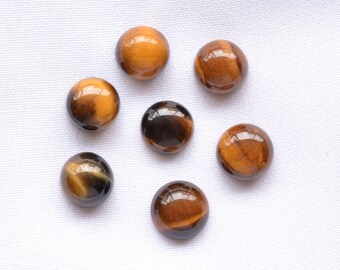 May include: Seven polished tiger's eye gemstone beads. The beads are round, with a glossy finish, and display a mix of golden brown and dark brown colors. The gemstones are arranged on a white surface.