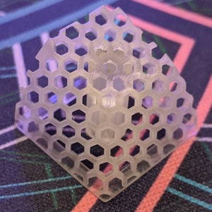 Peut inclure: Un objet en plastique transparent en forme de pyramide hexagonale. L'objet est fait d'un motif en nid d'abeille.
