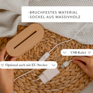 May include: A wooden lamp base with a built-in LED light strip. The lamp is connected to a white USB cable and a white power adapter with a European plug. The text on the image reads "BRUCHFESTES MATERIAL - SOCKEL AUS MASSIVHOLZ" and "Optional auch mit EU-Stecker" and "USB-Kabel".