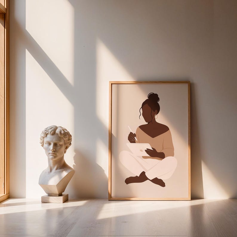 May include: A framed art print featuring a minimalist illustration of a person seated cross-legged, holding a stylus and tablet. The figure is depicted in shades of brown, beige, and white, with a light wood frame. A classical bust is also visible.