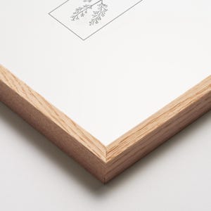 May include: A framed botanical print featuring a detailed black and white illustration of delicate plant sprigs. The artwork is set within a natural wood frame, showcasing the print's clean lines and minimalist aesthetic. The frame's light wood tone complements the artwork.