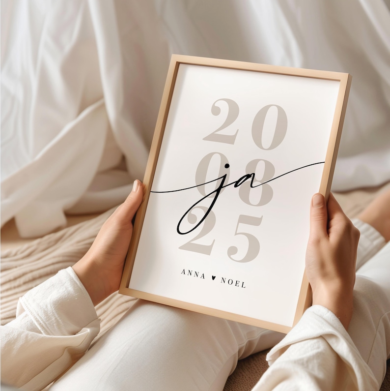 May include: A rectangular light wood frame containing a white print with large, light beige numbers 20 08 25 stacked vertically. The lowercase script letters ja are centered over the numbers, with the text ANNA &hearts; NOEL printed at the bottom.