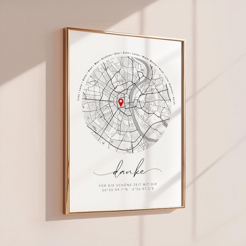 Puede incluir: Impresi&oacute;n enmarcada con un mapa en blanco y negro y un marcador rojo. La palabra "danke" est&aacute; escrita en cursiva debajo del mapa, junto con coordenadas y texto. El marco es dorado.