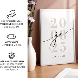 May include: A white framed wall art print featuring the large beige numbers 20 and 08 25 in the background. The word ja is written in a black cursive script across the center. At the bottom, the names Anna and Noel are separated by a small heart.