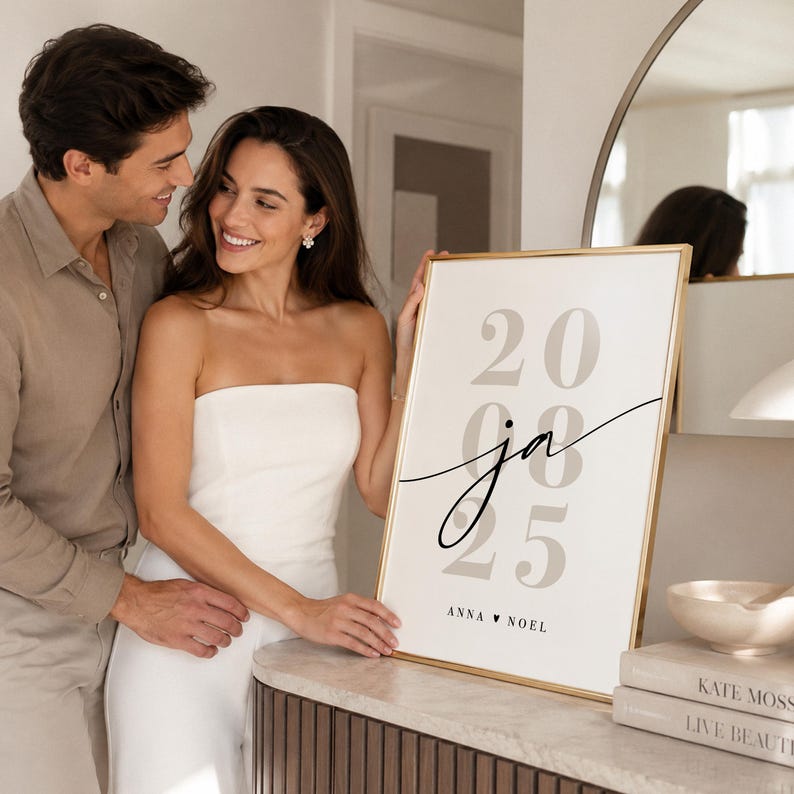May include: A rectangular framed print with a gold border featuring the large beige numbers 20, 08, and 25 stacked vertically. The black cursive letters ja are centered over the numbers, with the text ANNA &hearts; NOEL printed in black at the bottom.