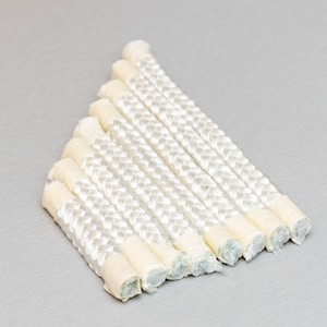 Könnte beinhalten: Eine Gruppe weißer geflochtener Schnüre mit einer beigefarbenen Ummantelung an den Enden. Die Schnüre sind fächerförmig angeordnet.