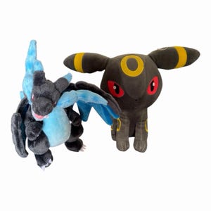 May include: Two plush toys: a black and blue dragon-like creature with blue flames and wings, and a dark gray creature with yellow accents and red eyes. Both are on a white background.