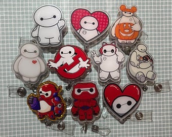 May include: A collection of ten acrylic badge reels featuring various illustrations of the white robot character Baymax. The designs include Baymax in different poses, wearing costumes, holding a cat, inside a heart, and in a red armor suit.