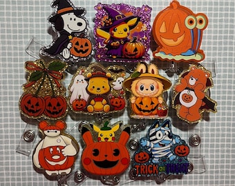 May include: A collection of ten acrylic badge reels featuring various cartoon characters in Halloween costumes, including Snoopy, Pikachu, Winnie the Pooh, and a mummy dog, all holding or surrounded by orange jack-o'-lantern pumpkins.