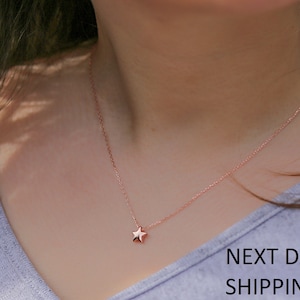 May include: A delicate rose gold necklace with a small star pendant. The necklace is on a model wearing a light gray shirt.