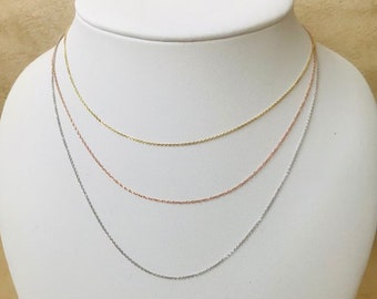 May include: Three delicate gold chains, one in yellow gold, one in rose gold, and one in white gold, are displayed on a white mannequin bust.