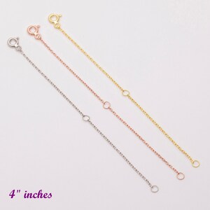 May include: Three gold chain extenders in different colors: yellow gold, rose gold, and white gold. Each extender is 4 inches long and has a lobster clasp on one end and a jump ring on the other end.